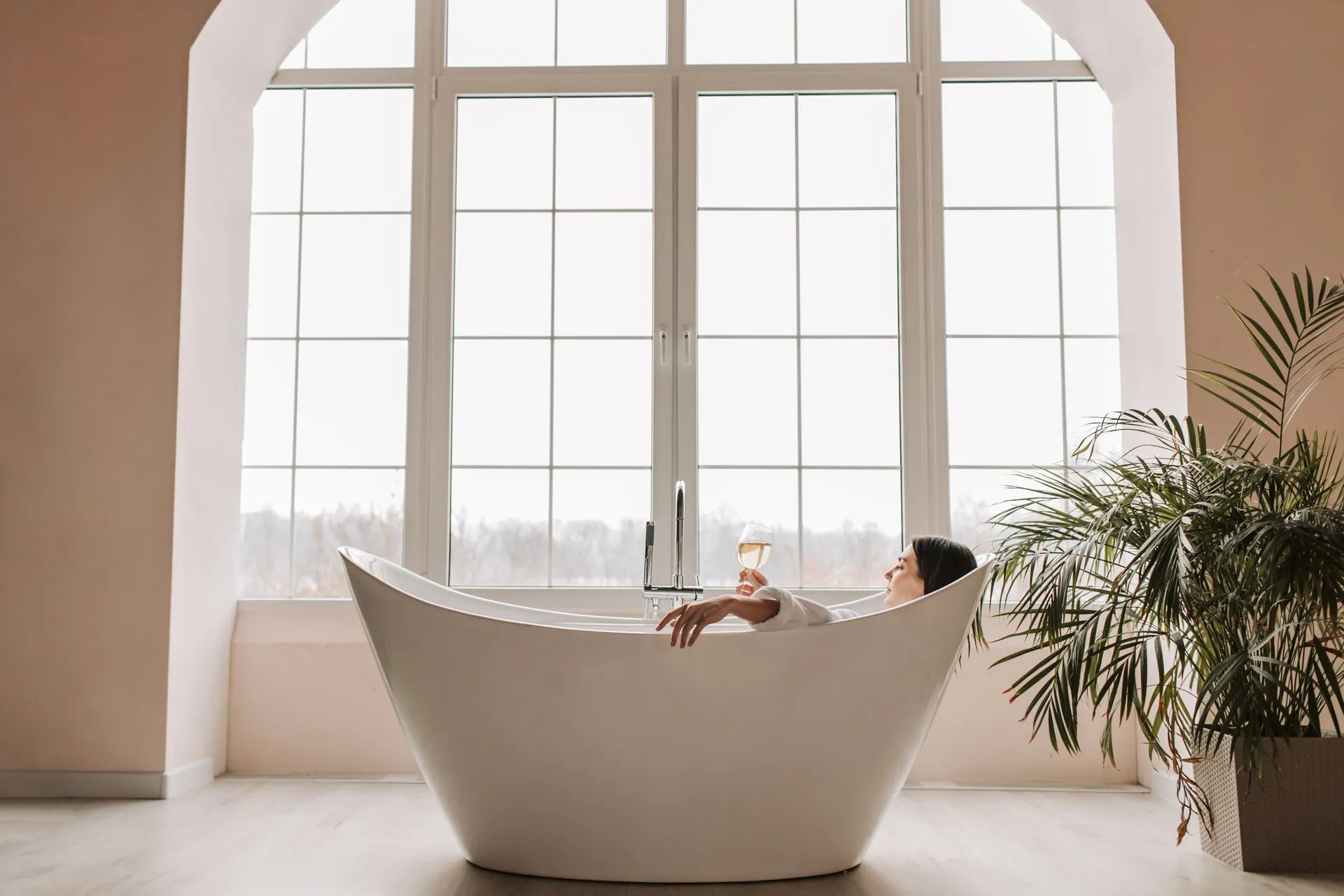 Woman relaxing in a freestanding bath by tall windows